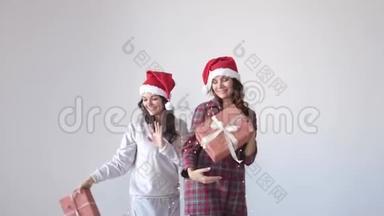 戴着圣诞帽的快乐女人在白色背景上用礼品盒跳舞。 假期概念